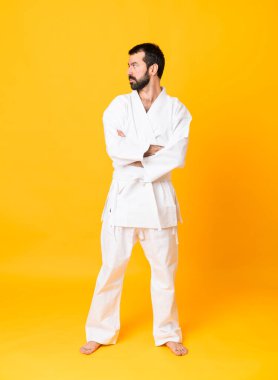 İzole edilmiş sarı arka planda kollarını çapraz tutarak karate yapan bir adamın tam boy fotoğrafı.