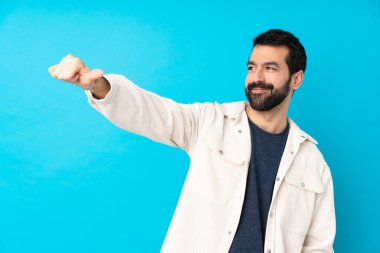 Beyaz kadife ceketli genç ve yakışıklı bir adam izole edilmiş mavi arka planda baş parmak işareti yapıyor.