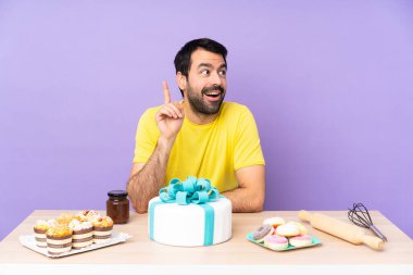 Masada elinde büyük bir pasta olan bir adam parmağını kaldıracak bir fikir düşünüyor.