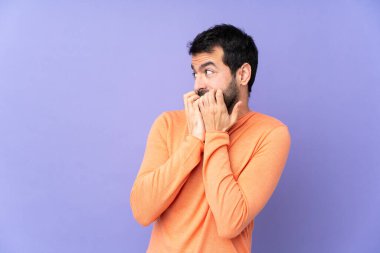 Mor arka planda beyaz tenli yakışıklı bir adam gergin ve korkmuş bir şekilde elleri ağıza veriyor.