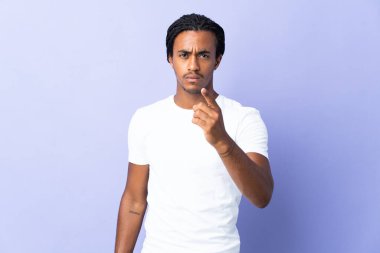 Örgülü genç Afrikalı Amerikalı adam mor arka planda izole edilmiş hayal kırıklığına uğramış ve ön tarafı işaret ediyor.