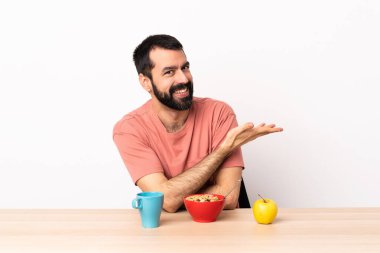 Masada kahvaltı yapan beyaz bir adam bir fikir sunuyor ve gülümsüyor..