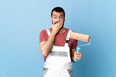 Yetişkin ressam, izole edilmiş mavi arka planda elleriyle ağzını kapatıyor.