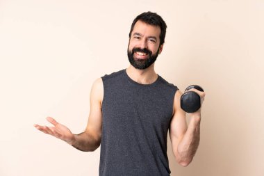 Sakallı, beyaz tenli bir sporcu izole edilmiş arka planda ağırlık kaldırıyor ve gülümsüyor.