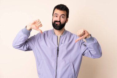 Sakallı, ceketli, soyutlanmış arka planda beyaz bir adam baş parmağını iki eliyle aşağı gösteriyor.