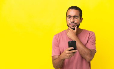 Genç Latin adam sarı arka planda izole edilmiş düşünüyor ve bir mesaj gönderiyor.