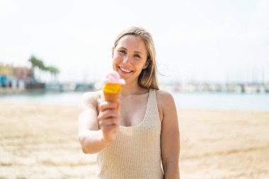 Açık havada kornet dondurmalı genç sarışın kadın, neşeli bir ifadeyle.