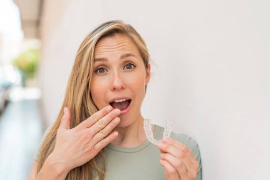 Açık havada sarışın bir kadın. Elinde, şaşırmış bir ifadeyle görünmez diş telleri var.