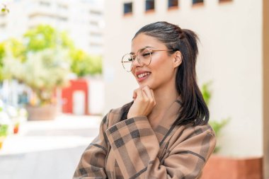 Dışarıda gözlüklü genç bir kadın yan tarafa bakıyor.