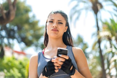 Dışarıda cep telefonu kullanan genç ve güzel bir bayan. Üzgün bir ifadeyle.