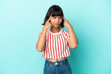 Genç melez kadın, mavi arka planda izole edilmiş. Şüpheleri ve düşünceleri var.