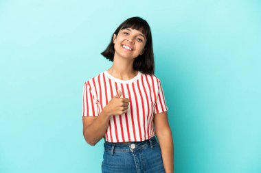 Mavi arka planda izole edilmiş genç melez bir kadın baş parmak işareti yapıyor.