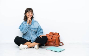 Genç bir kız öğrenci, beyaz arka planda tek başına oturmuş, yan tarafa bakıyor.