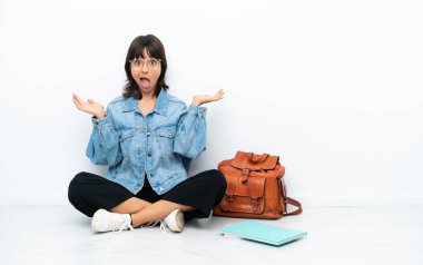 Genç bir kız öğrenci, beyaz arka planda izole bir şekilde oturuyor. Yüzünde şok ifadesi var.