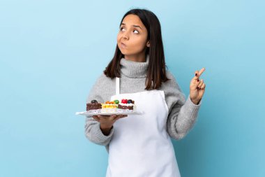 Pasta şefi, izole edilmiş mavi arka planda büyük bir pasta tutuyor ve en iyisini diliyor..