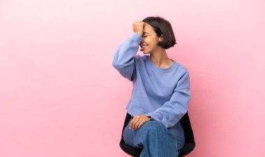 Pembe arka planda izole edilmiş bir sandalyede oturan genç melez kadın bir şeyin farkına vardı ve çözüme niyetlendi.