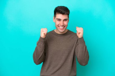 Mavi arka planda izole edilmiş genç beyaz adam galibiyeti kutluyor.