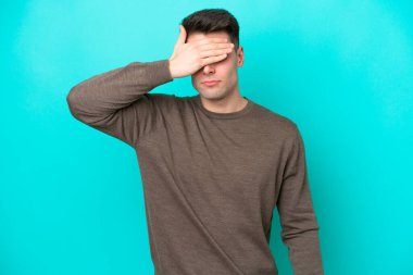 Genç beyaz adam mavi arka planda tek başına, gözleri elle kapatıyor. Bir şey görmek istemiyorum.