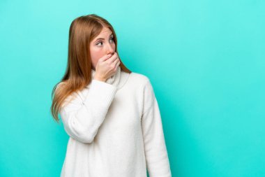 Genç kızıl saçlı kadın mavi arka planda izole edilmiş. Yan tarafa bakarken sürpriz jest yapıyor.