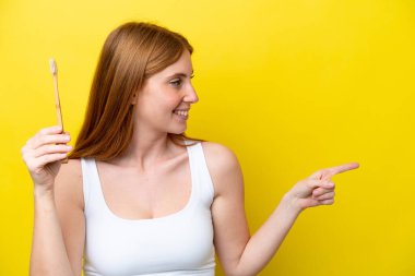 Genç kızıl saçlı, dişlerini fırçalayan kadın bir ürün sunmak için kenarı işaret ediyor.