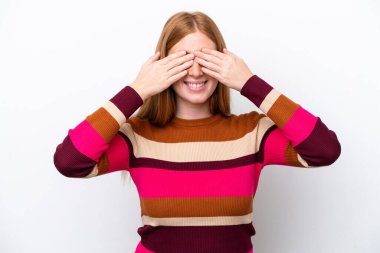 Genç kızıl saçlı kadın beyaz arka planda izole edilmiş gözleri elleriyle kaplayan ve gülümseyen.