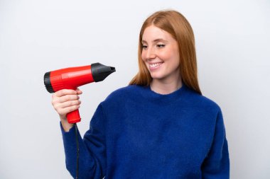 Kızıl saçlı genç bir kadın elinde saç kurutma makinesiyle beyaz arka planda mutlu bir ifadeyle izole edilmiş.