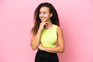 Pembe arka planda izole edilmiş genç İspanyol kadın yana bakıyor ve gülümsüyor.