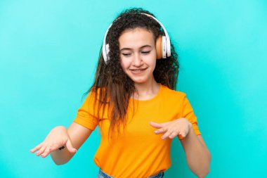Genç Arap kadın mavi arka planda izole edilmiş müzik ve dans dinliyor.
