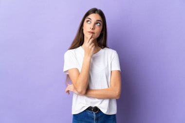 Kafkasyalı genç bir kadın mavi arka planda izole edilmiş, yukarı bakarken şüpheleri var.