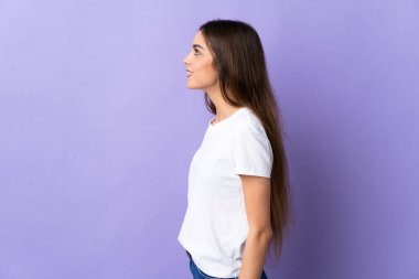 Genç beyaz kadın mavi arka planda izole edilmiş. Yan pozisyonda gülüyor.