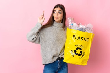 Pembe arka planda izole edilmiş plastik şişelerle dolu bir çanta taşıyan beyaz bir kadın.