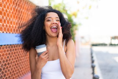 Genç Afrikalı Amerikalı bir kadın açık havada kahve alıp, ağzı açık bağırıyor.