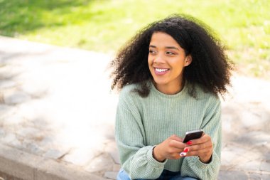 Açık havada cep telefonu kullanan genç Afrikalı Amerikalı kadın.