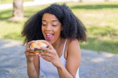 Genç Afrikalı Amerikalı kadın elinde hamburgerle dışarıda