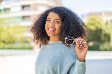 Dışarıda gözlüklü genç Afrikalı Amerikalı kadın çok gülümsüyor.