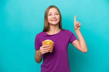 Mavi arka planda izole edilmiş patates kızartması yiyen genç Rus kadın harika bir fikre işaret ediyor.