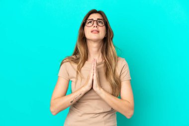 Mavi arka planda izole edilmiş genç beyaz kadın avuç içlerini bir arada tutuyor. İnsan bir şey ister.