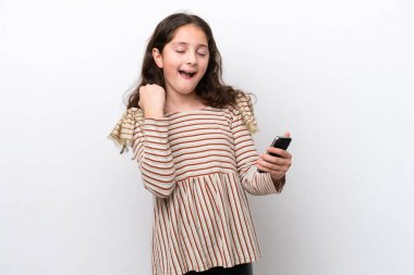 Küçük kız beyaz arka planda izole edilmiş ve telefon zafer pozisyonunda.