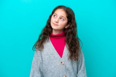 Mavi arka planda izole edilmiş küçük bir kız yukarı bakarken bir fikir düşünüyor.