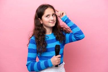 Küçük şarkıcı kız pembe arka planda izole edilmiş bir mikrofonu kaldırdı. Şüpheleri vardı ve kafası karışmıştı.