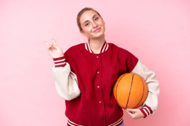 Genç basketbolcu beyaz kadın pembe arka planda izole edilmiş gülümsüyor ve zafer işareti gösteriyor.