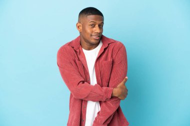 Genç latin adam mavi arka planda yalnız gülüyor.