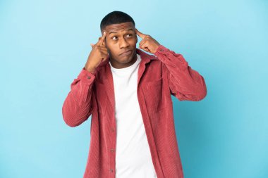 Genç Latin bir adam mavi arka planda izole edilmiş. Şüpheleri ve düşünceleri var.