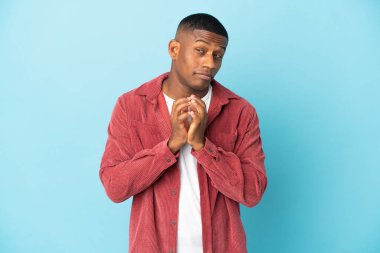 Genç latin adam mavi arka planda bir şeyler planlıyor.