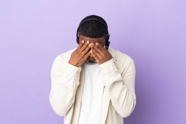 Mor arka planda, yorgun ve hasta bir ifadeyle izole edilmiş bir kulaklıkla çalışan pazarlamacı Latin bir adam.