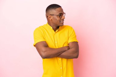 Pembe arka planda izole edilmiş genç Latin adam mutlu ve gülümsüyor.