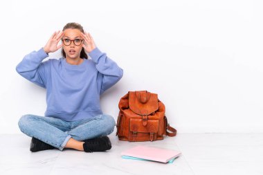 Genç öğrenci kız, beyaz arka planda, şaşırtıcı bir ifadeyle tek başına oturuyor.