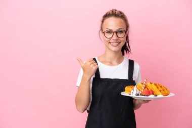 Pembe arka planda gözleme tutan Rus garson kız bir ürünü sunmak için yan tarafı işaret ediyor.