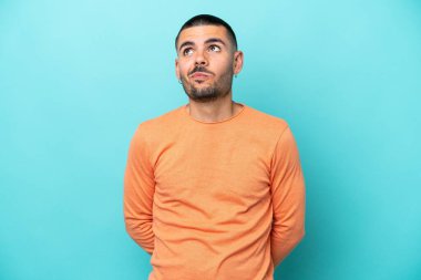 Kafkasyalı genç adam mavi arka planda izole edilmiş ve yukarı bakıyor.