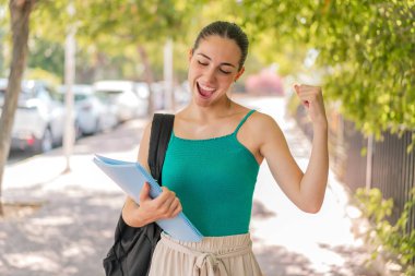 Dışarıda zaferi kutlayan genç ve güzel bir bayan öğrenci.